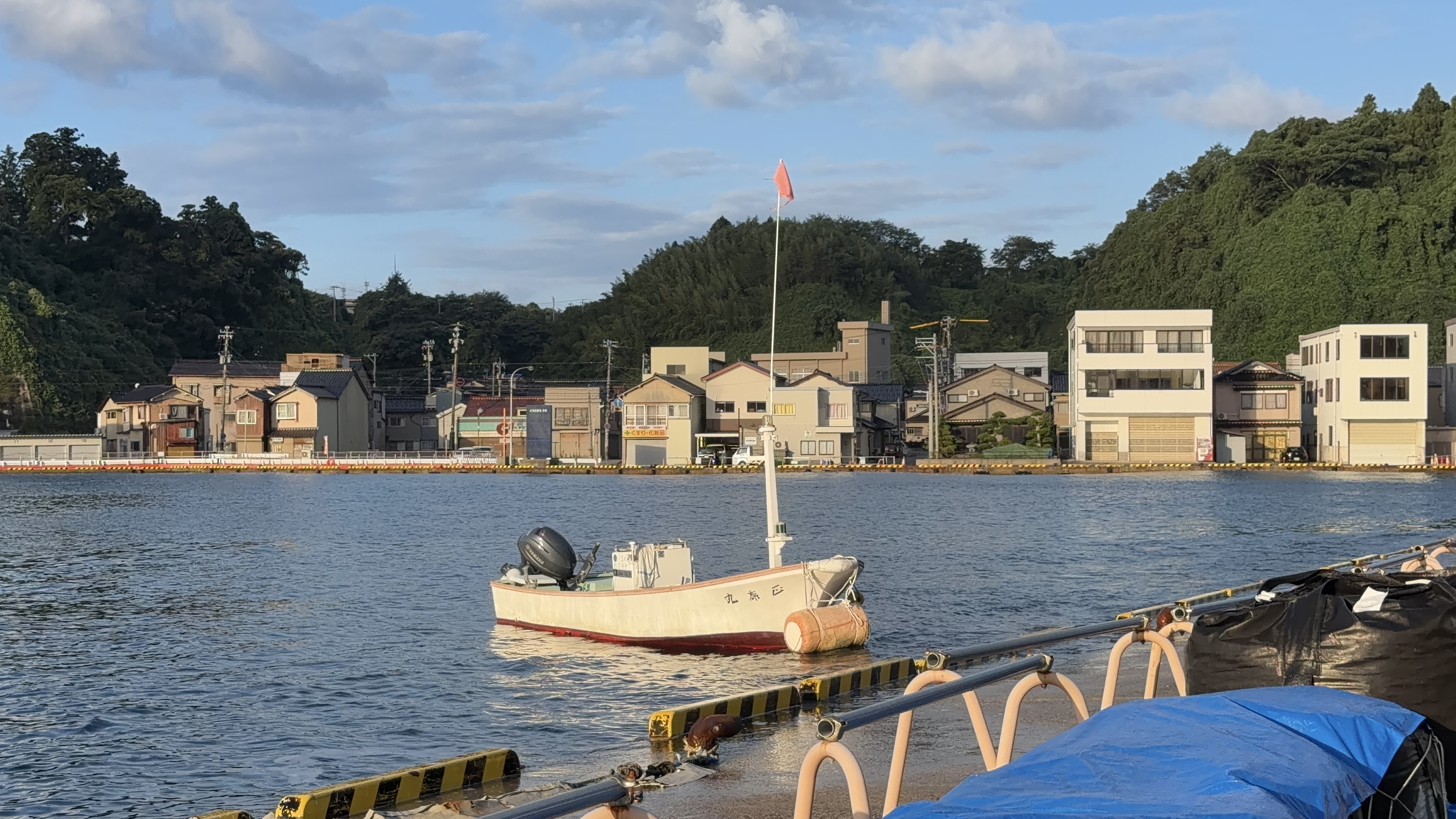係留された白い小舟と、朝日に照らされる対岸の住宅街