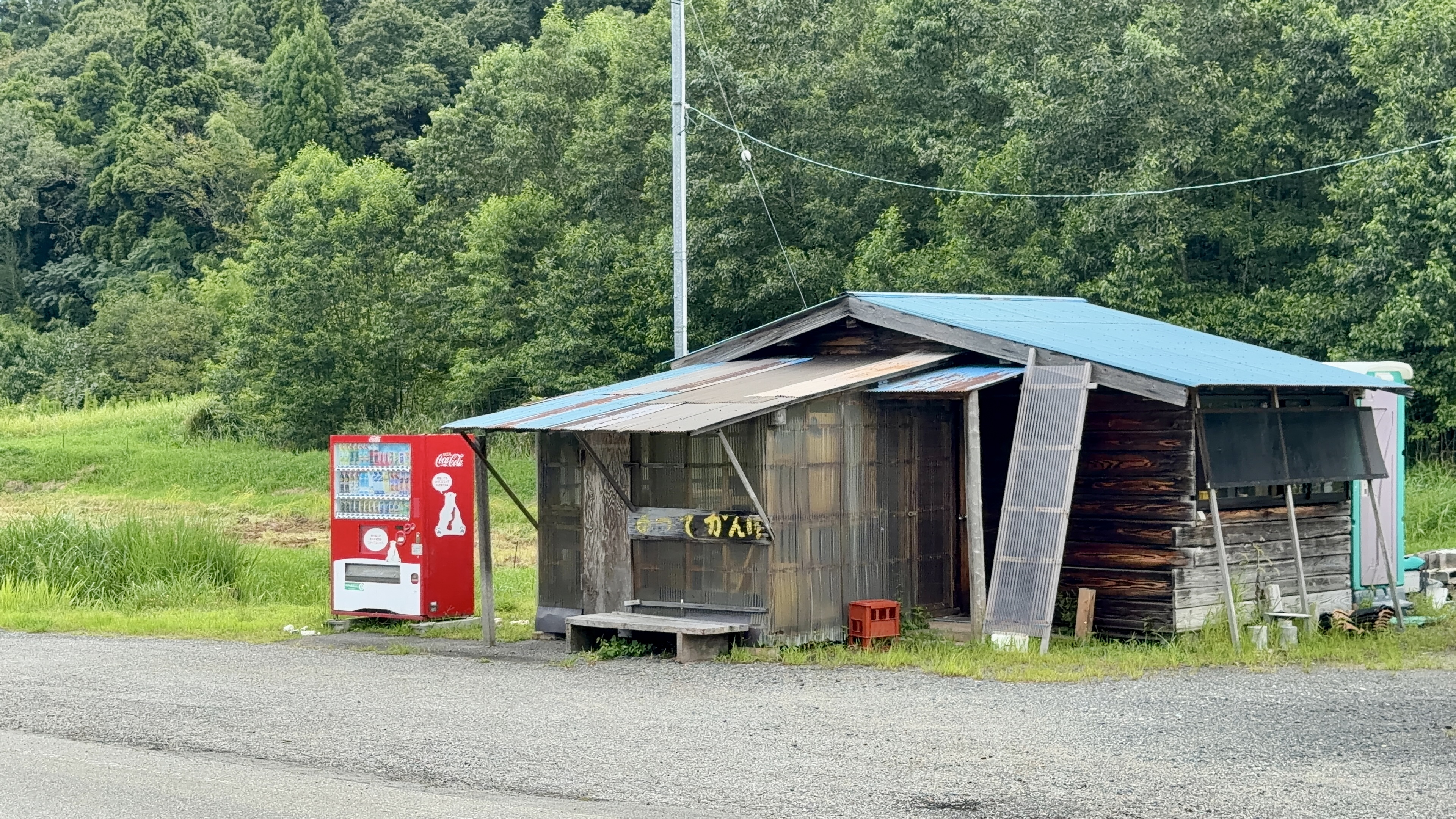 「よってかんけ」の看板がかかる木造の小屋と自動販売機