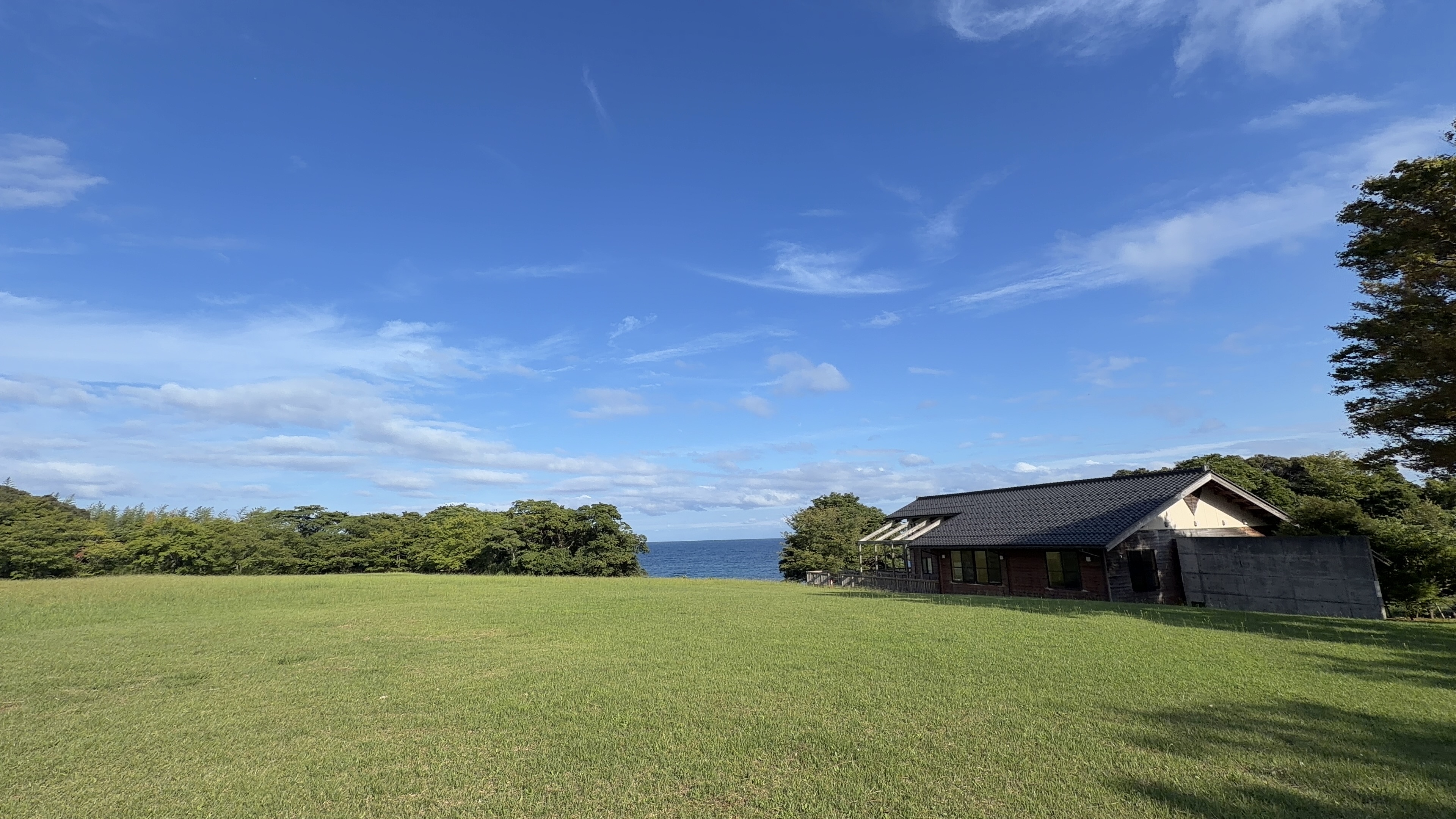 青空の下、広々とした芝生広場とのと海洋ふれあいセンターの建物、その先に広がる青い海