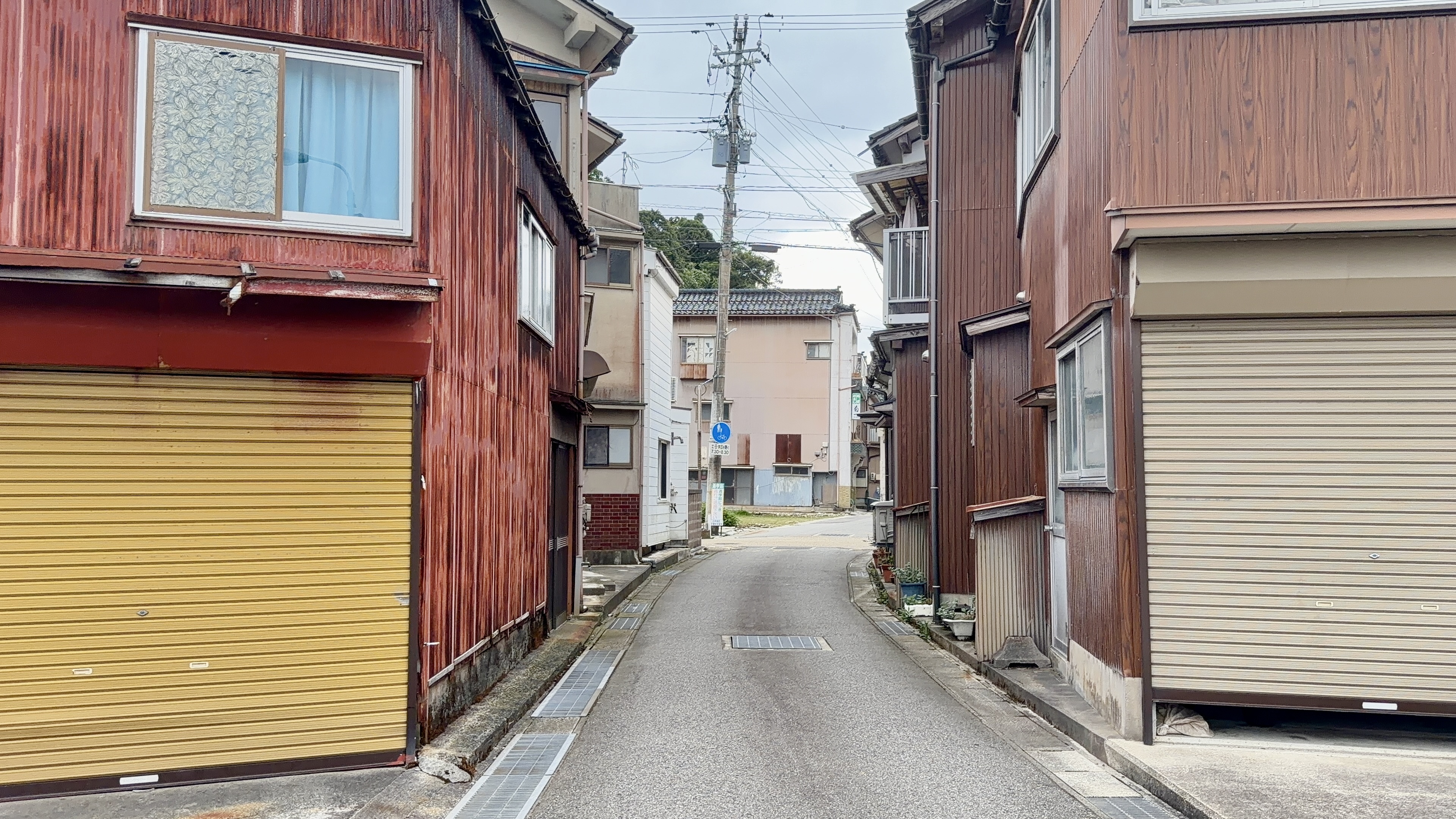 赤いトタン壁と黄色いシャッターが並ぶ、小木の住宅街の路地