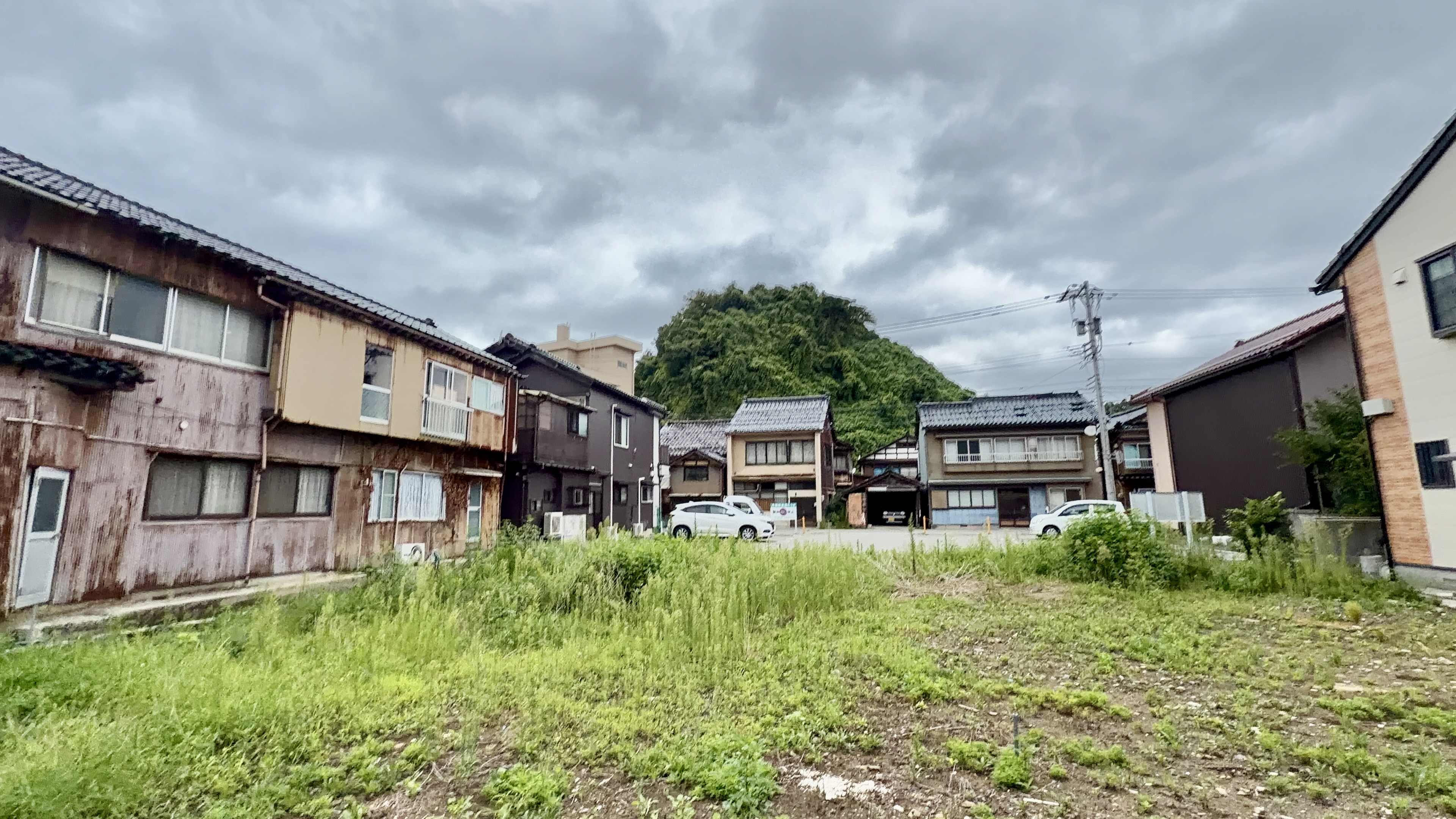 古い木造家屋と新しい住宅が入り混じる小木の住宅街、駐車場と空き地の風景