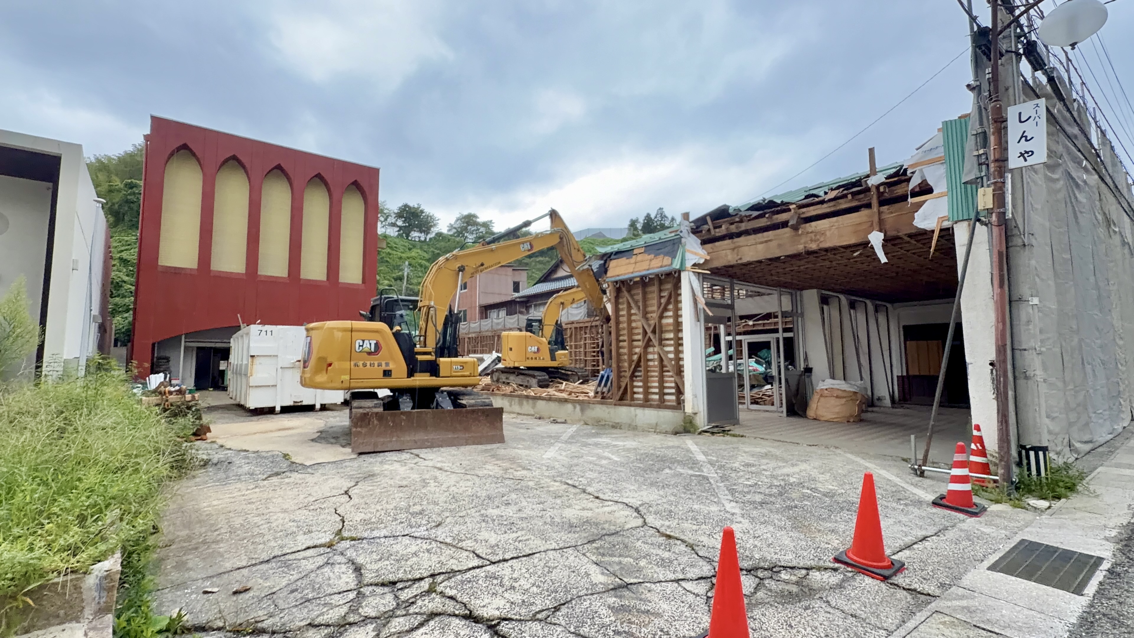 アーチ型の窓が並ぶ赤い壁の建物と、解体作業中の黄色いショベルカー2台