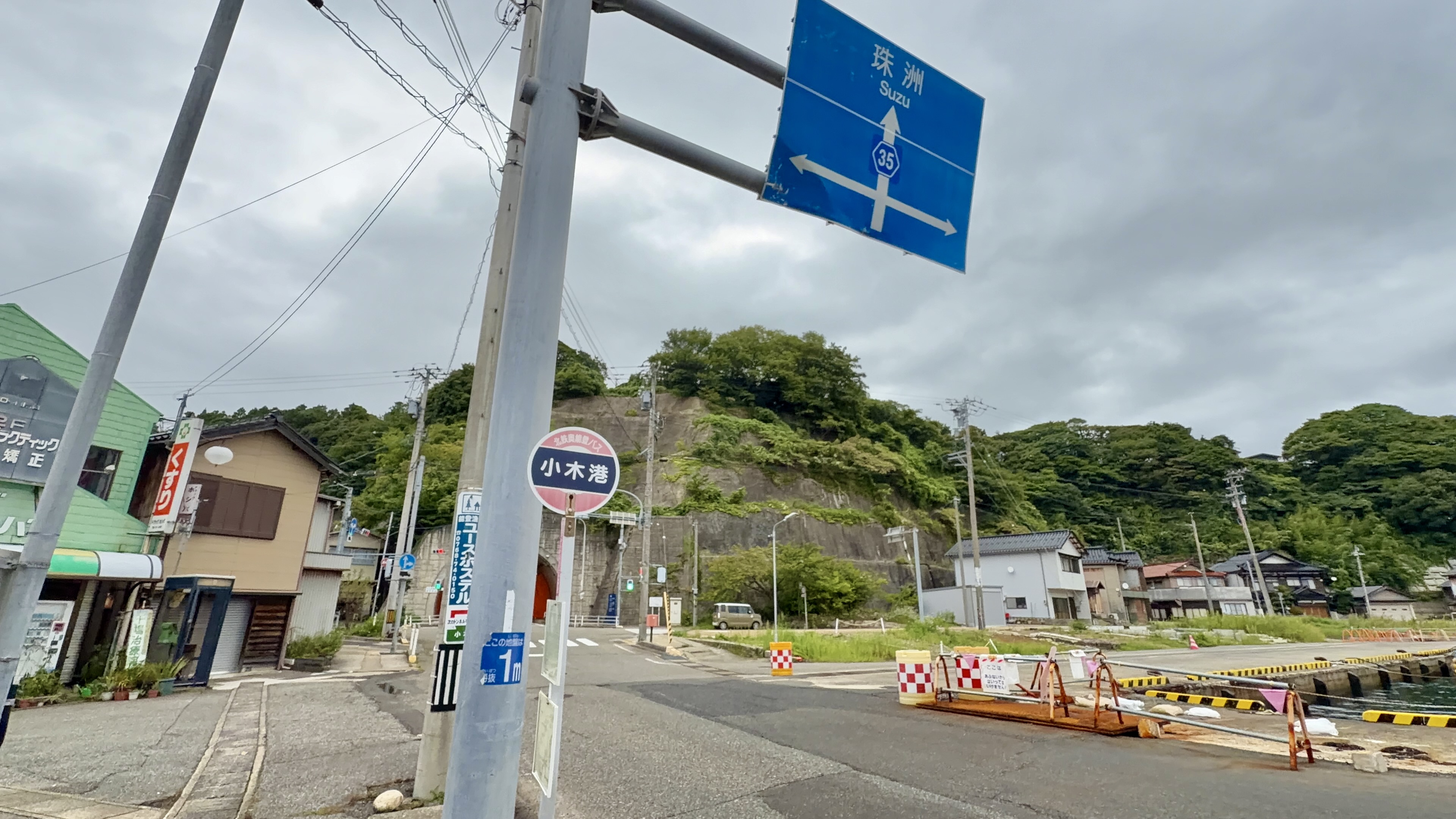 珠洲方面への案内標識と「小木港」バス停、奥にトンネルの見える戻り道