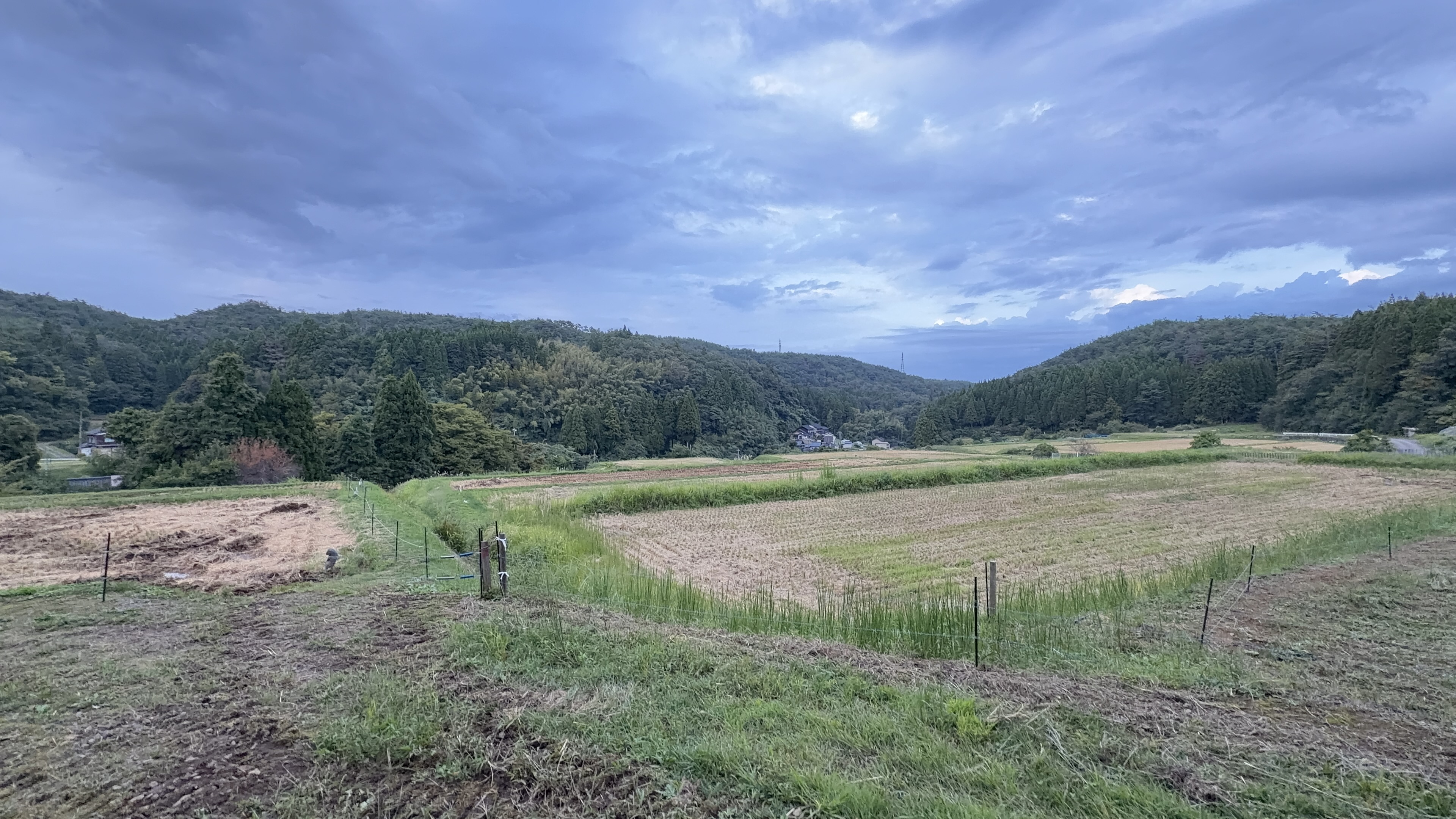 幾重にも重なる山並みのシルエット、夕暮れの雲が広がる空の下、田んぼが広がる
