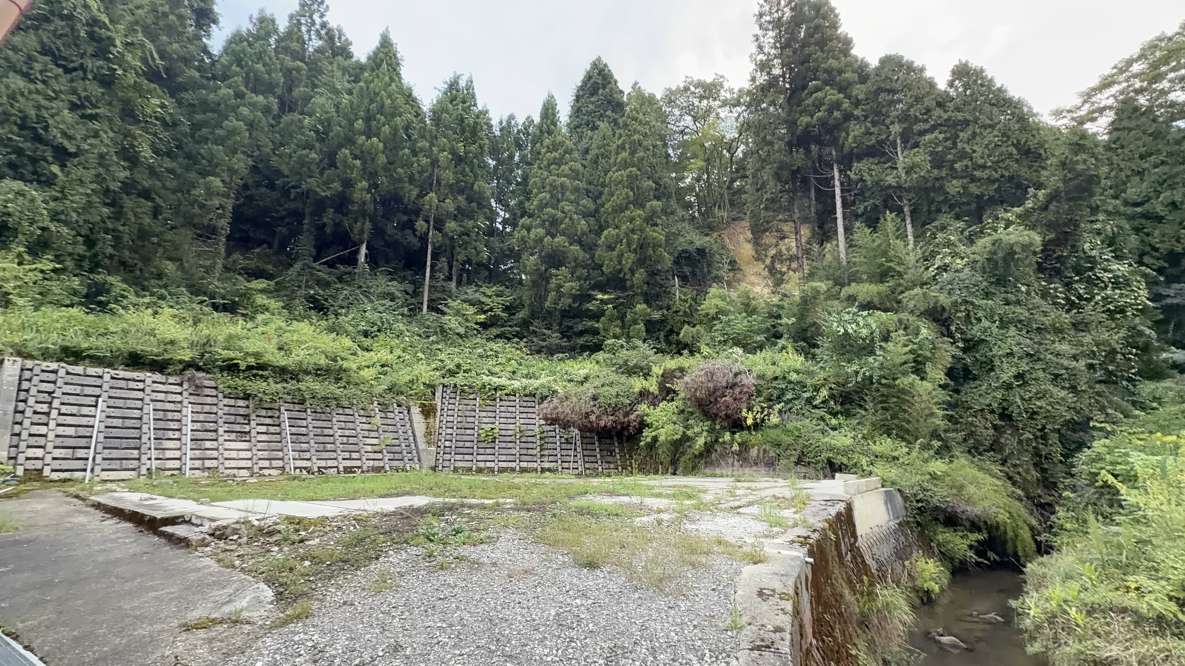 コンクリートブロックの擁壁と、奥の山肌にうっすら見える土の色、曇った夕方の空