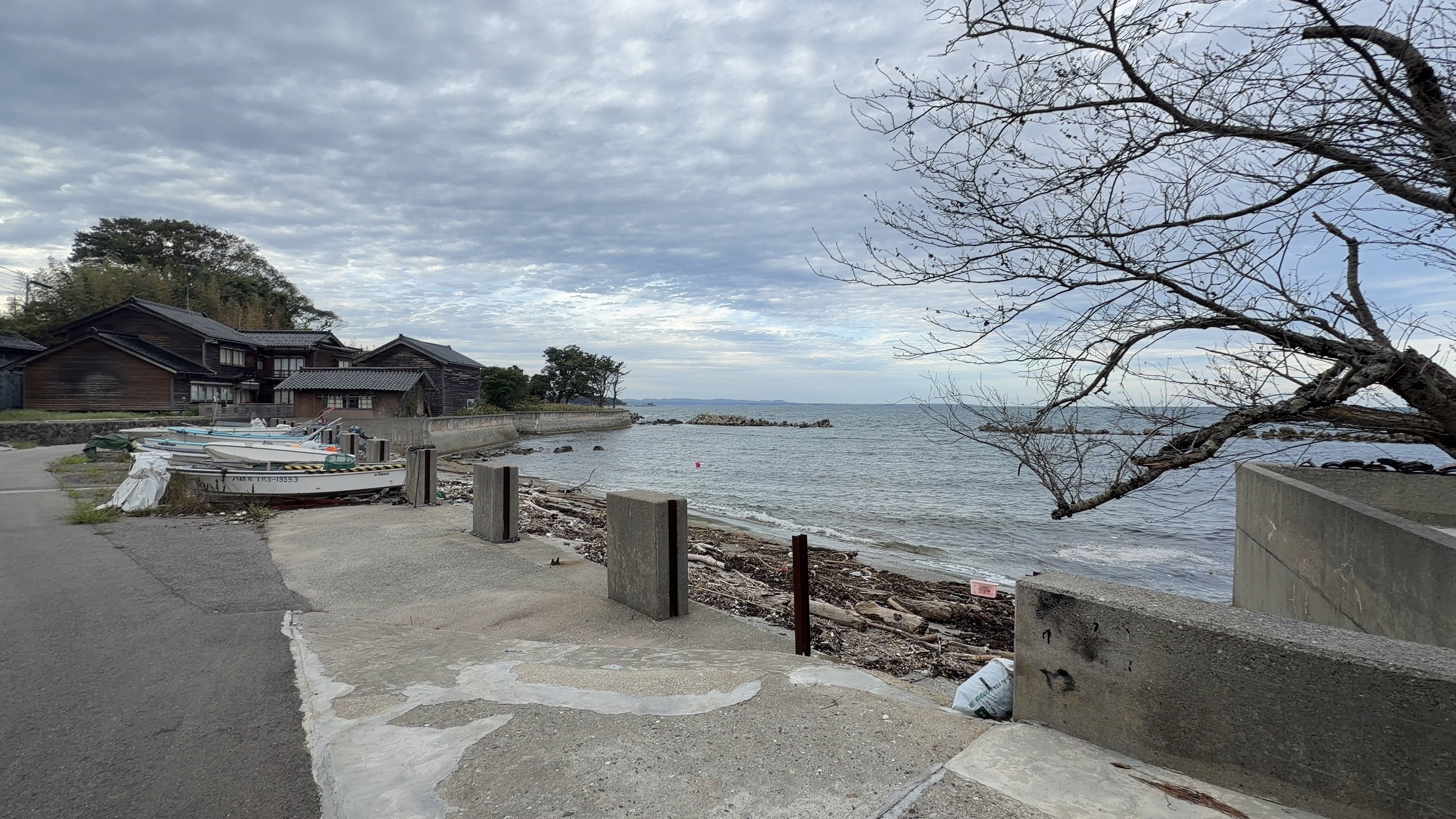 立壁の海岸、係留されたボートと木造家屋の先に広がる能登の海、遠くに岬
