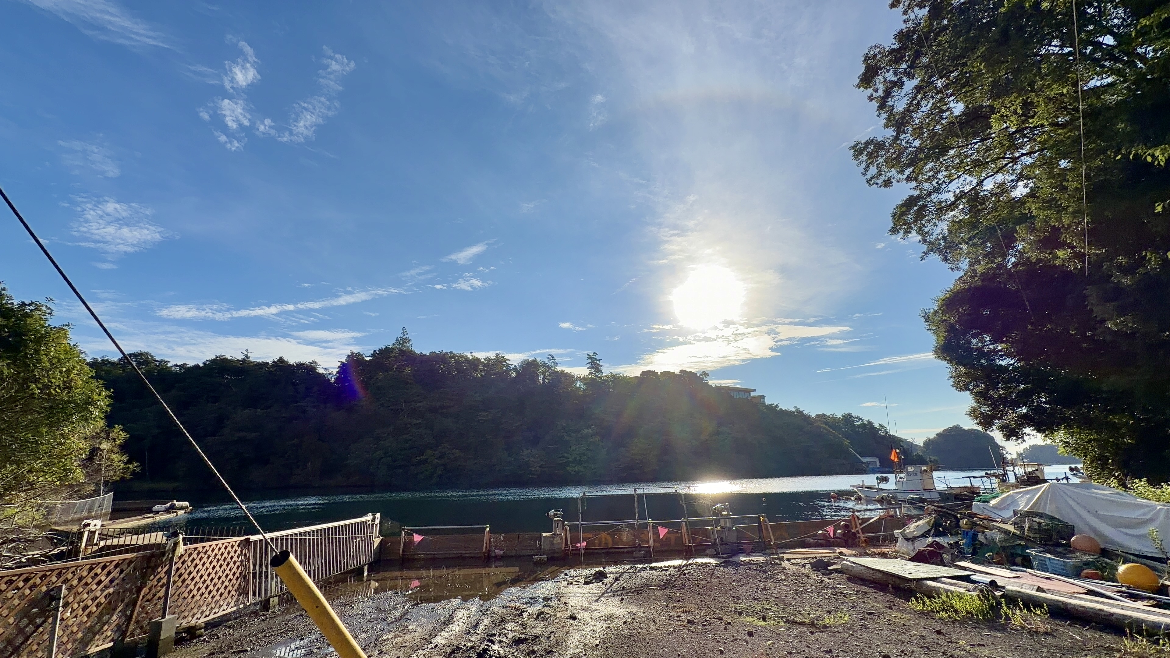 逆光にきらめく穏やかな湾、左手に崖の上の建物、正面に朝日、右手に緑の岬