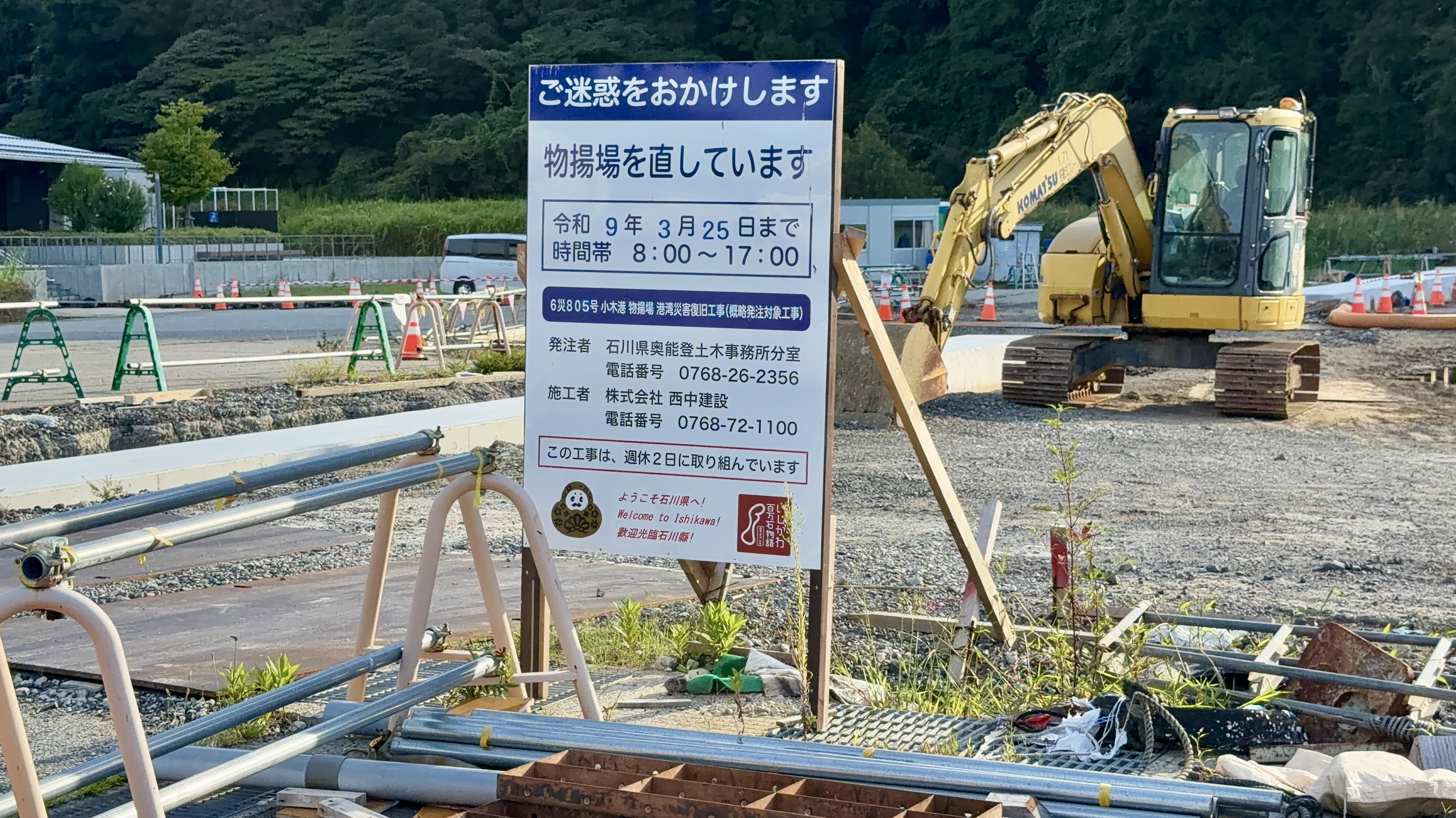 「ご迷惑をおかけします 物揚場を直しています」と書かれた工事看板、奥に重機とプレハブ小屋